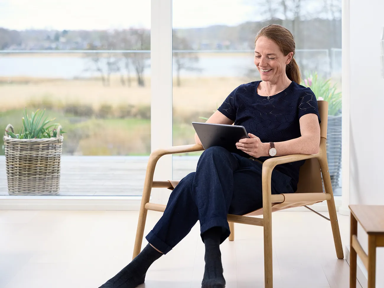 Kvinde sidder i en stol og bruger sin tablet mens hun smiler