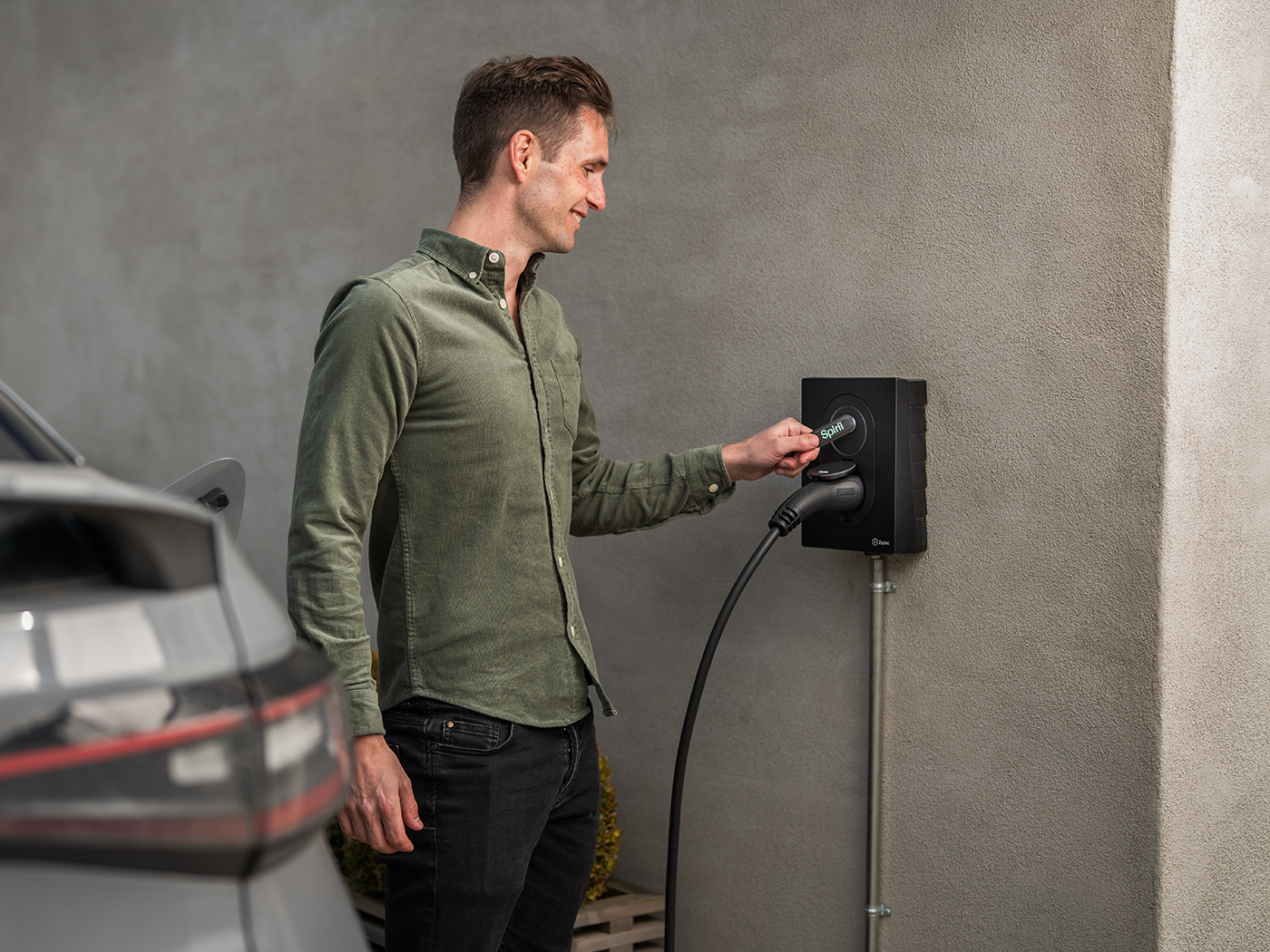 Mand står og smiler mens han anvender Spirii ladebrik på ladeboks for opladning af elbil