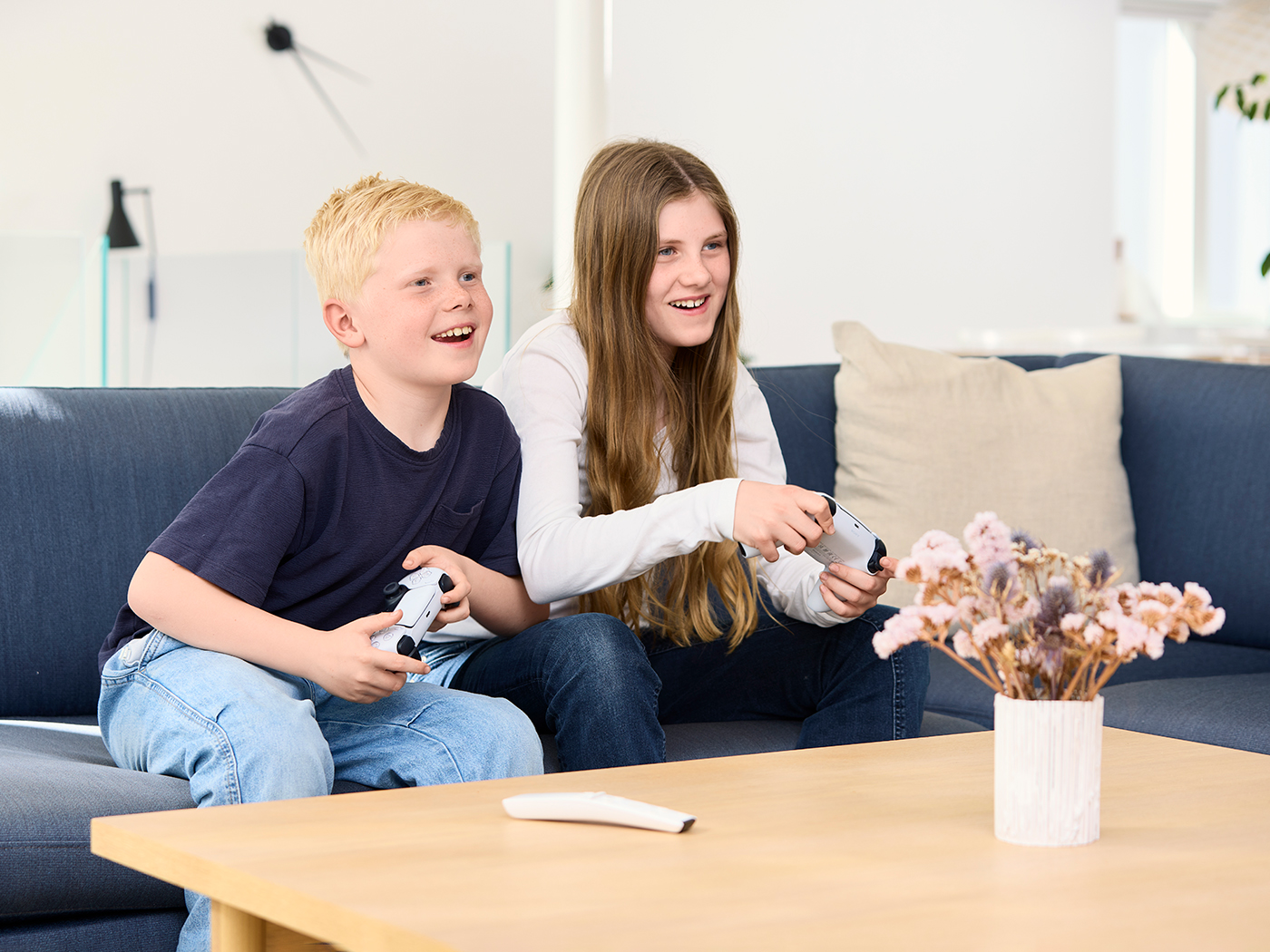 Dreng og pige sidder i sofaen og spiller konsolspil de koncentrerer sig om spillet