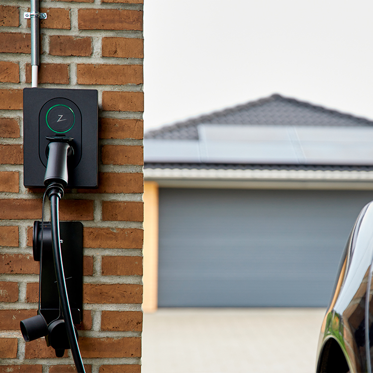 Ladeboks monteret på rød murstensvæg oplader elbil, i baggrunden ses garagetag med solceller monteret på taget