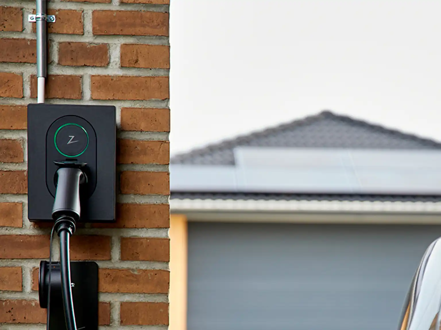 Ladeboks monteret på rød murstensvæg oplader elbil, i baggrunden ses garagetag med solceller monteret på taget
