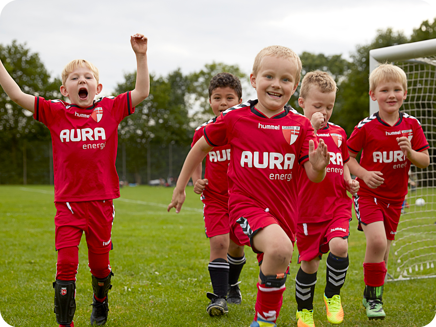 5 drenge der jubler i fodboldtøj sponsoreret af AURA på fodboldbane