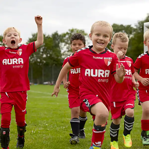 5 drenge der jubler i fodboldtøj sponsoreret af AURA på fodboldbane