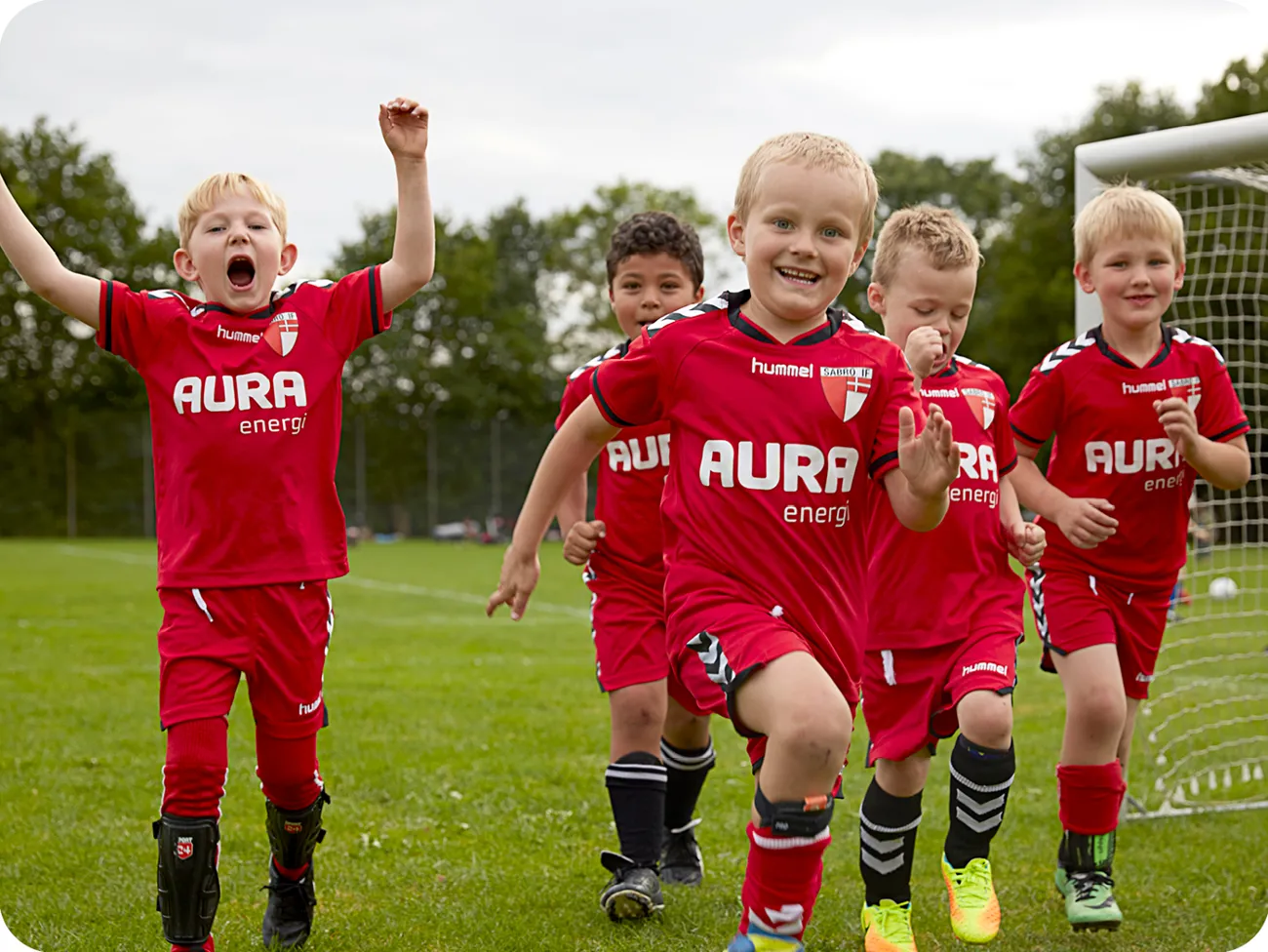5 drenge der jubler i fodboldtøj sponsoreret af AURA på fodboldbane