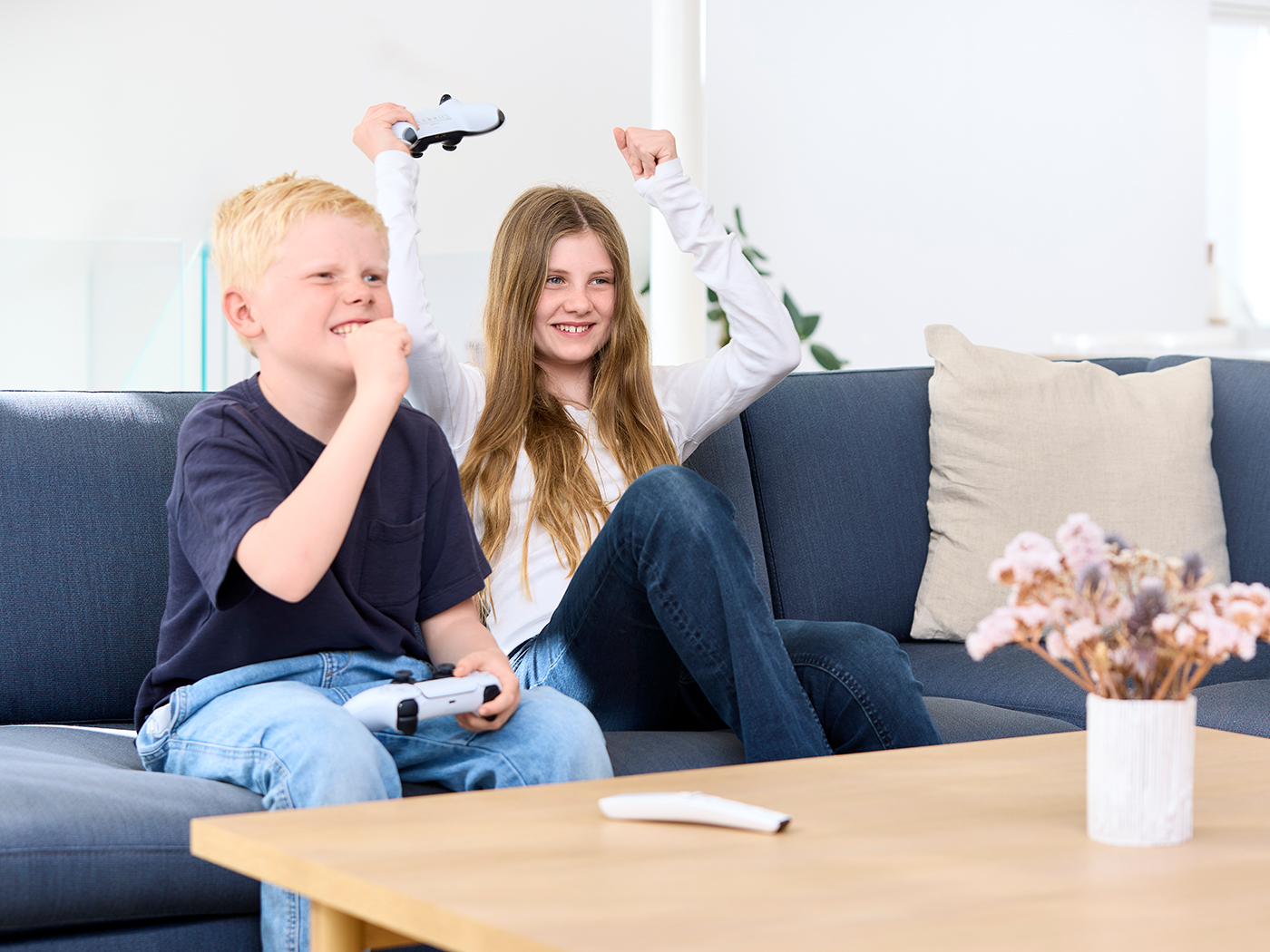 Dreng og pige sidder i sofaen og spiller konsolspil de jubler med hænderne over hovedet