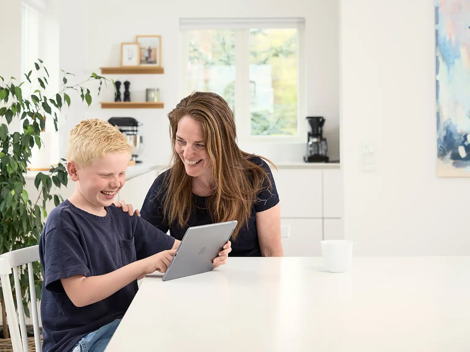 Mor og søn sidder sammen ved spisebordet og griner med deres tablet