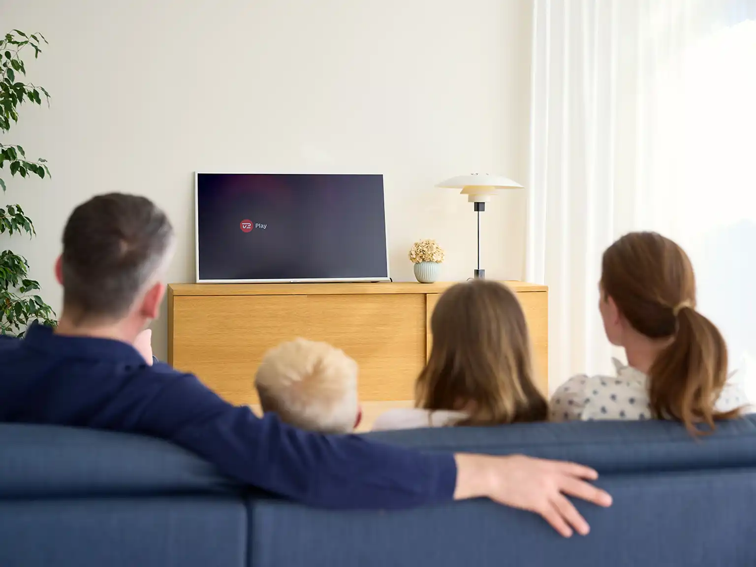 Familie sidder sammen i en sofa de streamer TV 2 Play på tvet