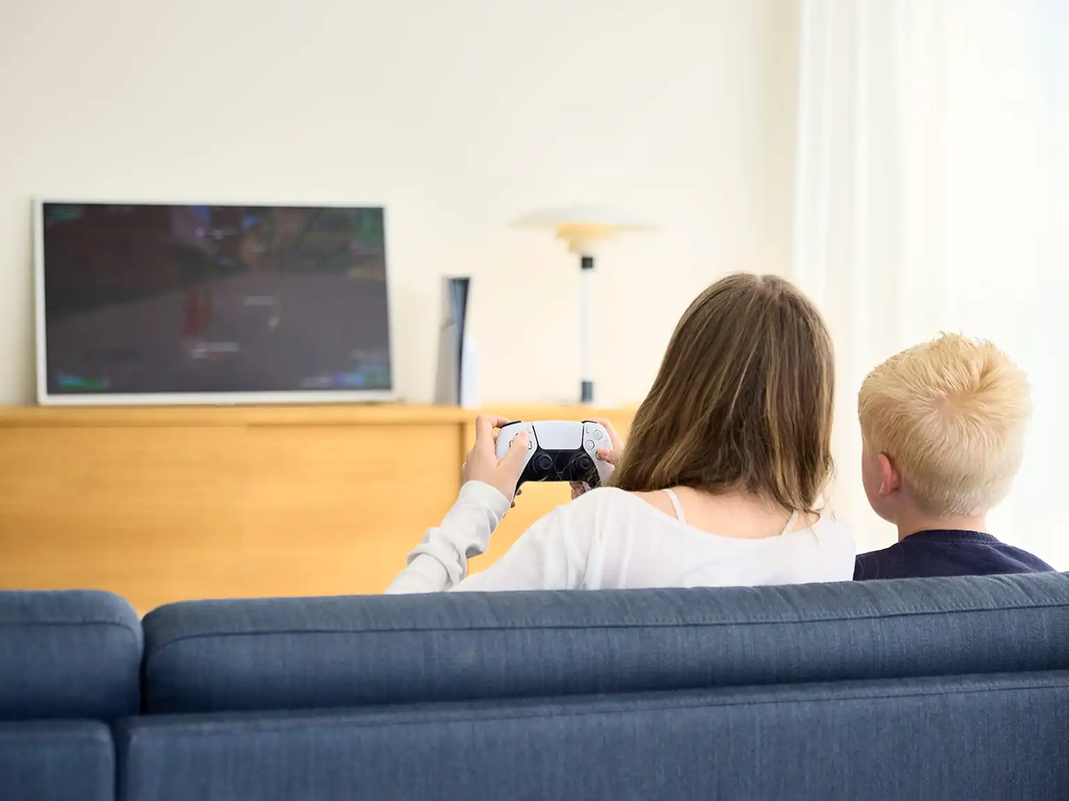Pige holder kontroller og spiller mens drengen kigger på