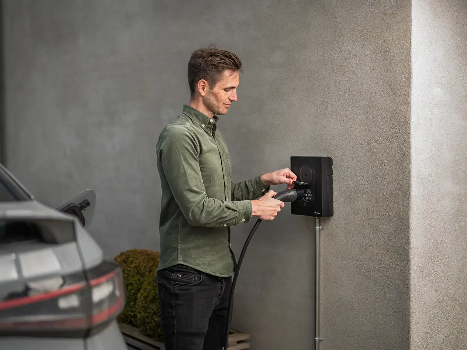 Mand der sætter ladekabel i ladestikket for at oplade elbil