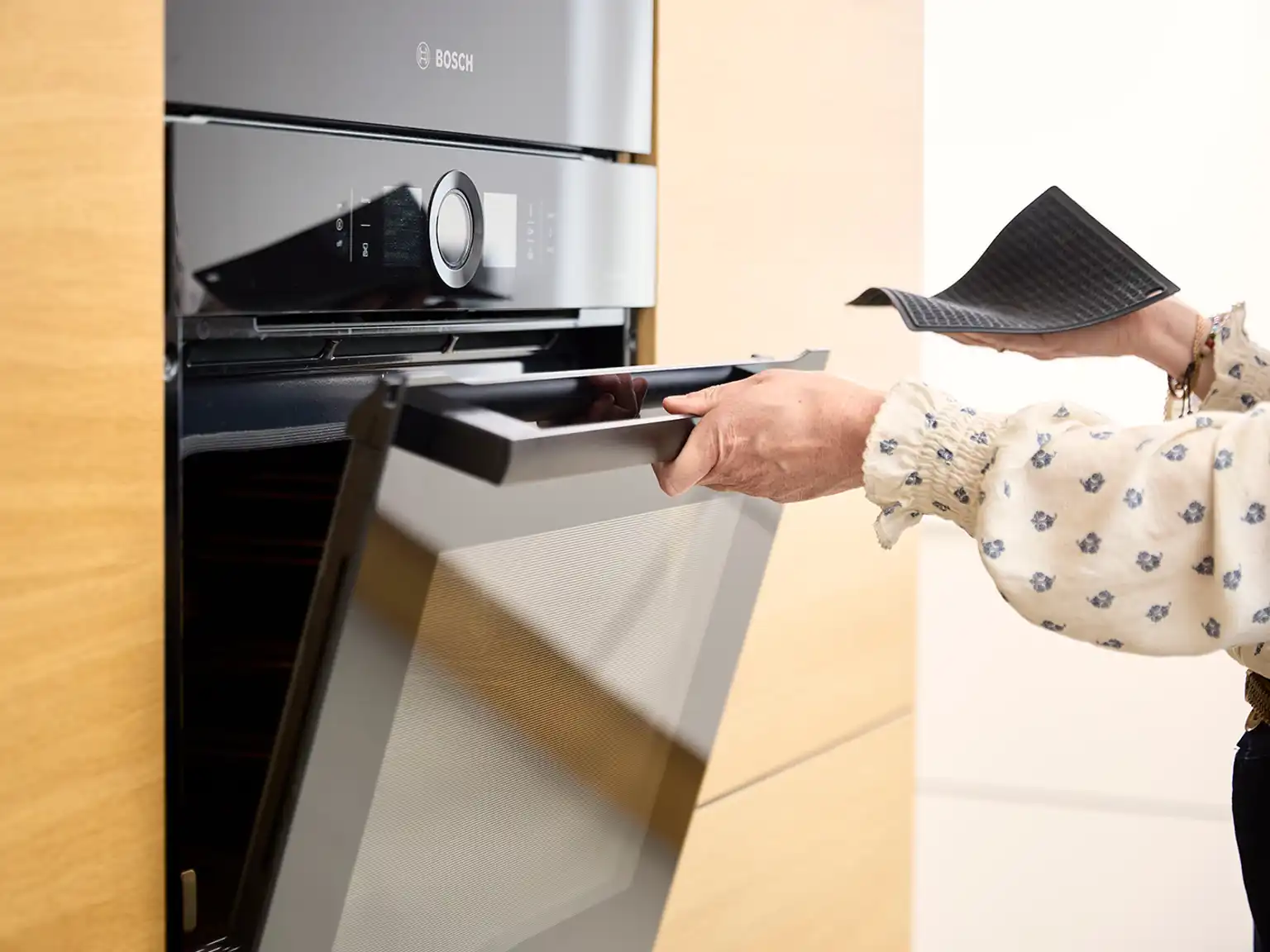 Kvinde åbner ovn mens hun holder en grydelap i den anden hånd