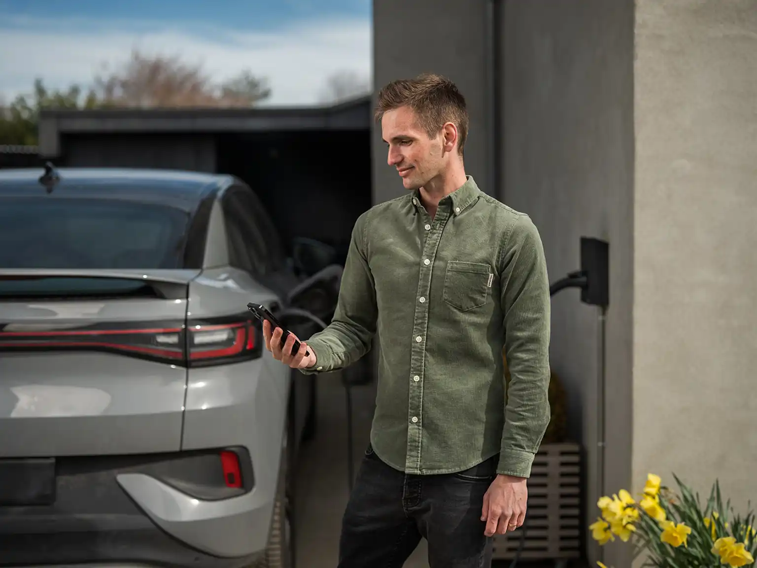 Mand står med sin mobil i hånden mens elbilen lader