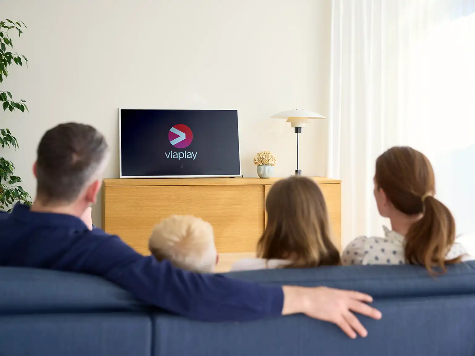 Familie sidder sammen i en sofa de streamer Viaplay på tvet