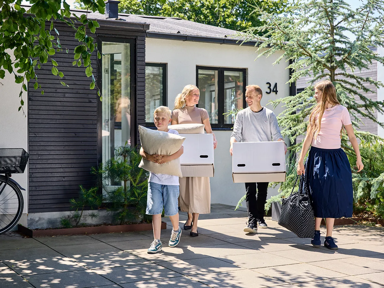 Familie på to voksne og to børn går med flyttekasser og oppakning fra hus