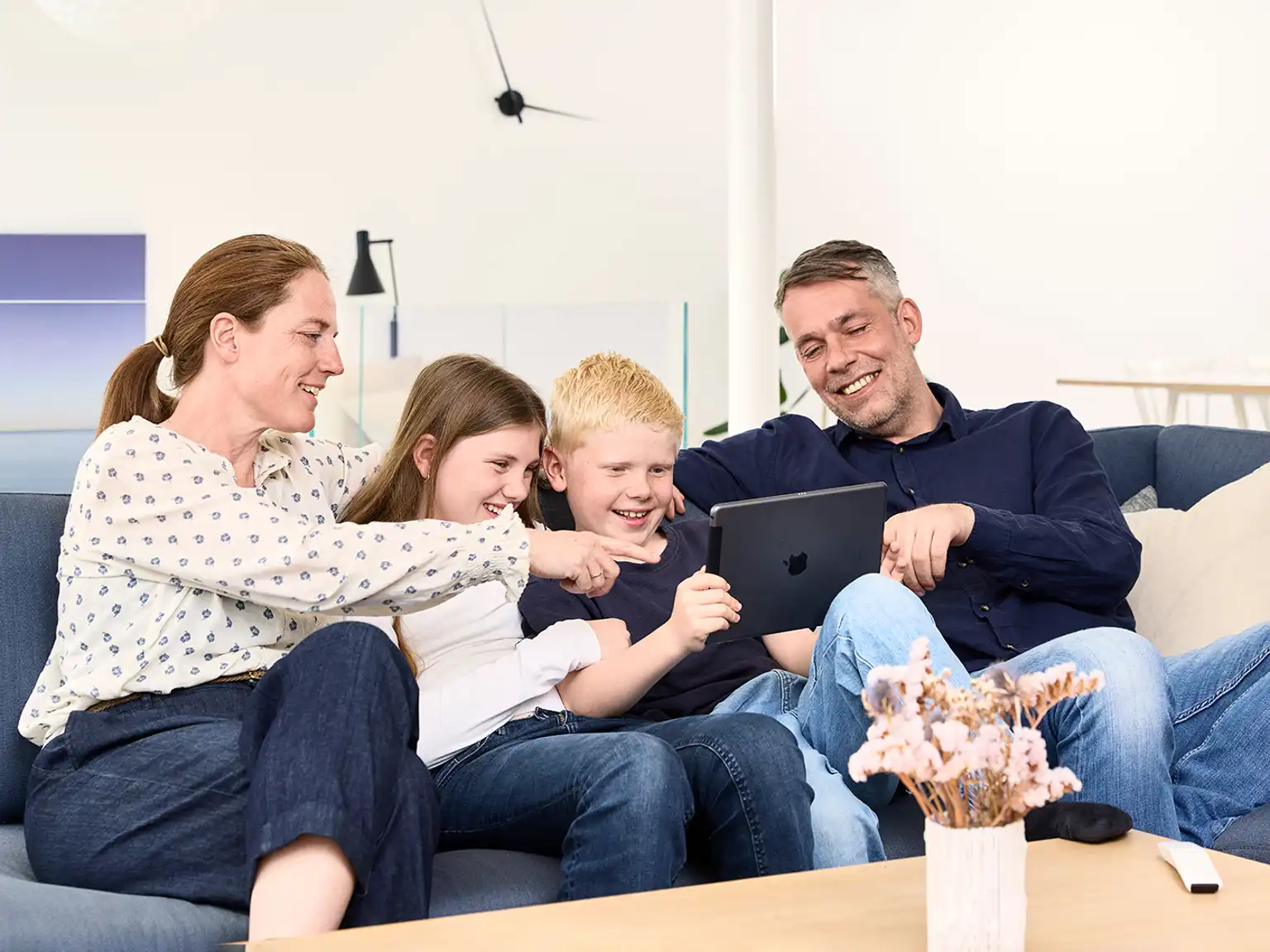 Familie sidder sammen i sofa drengen holder en tablet som de alle kigger på