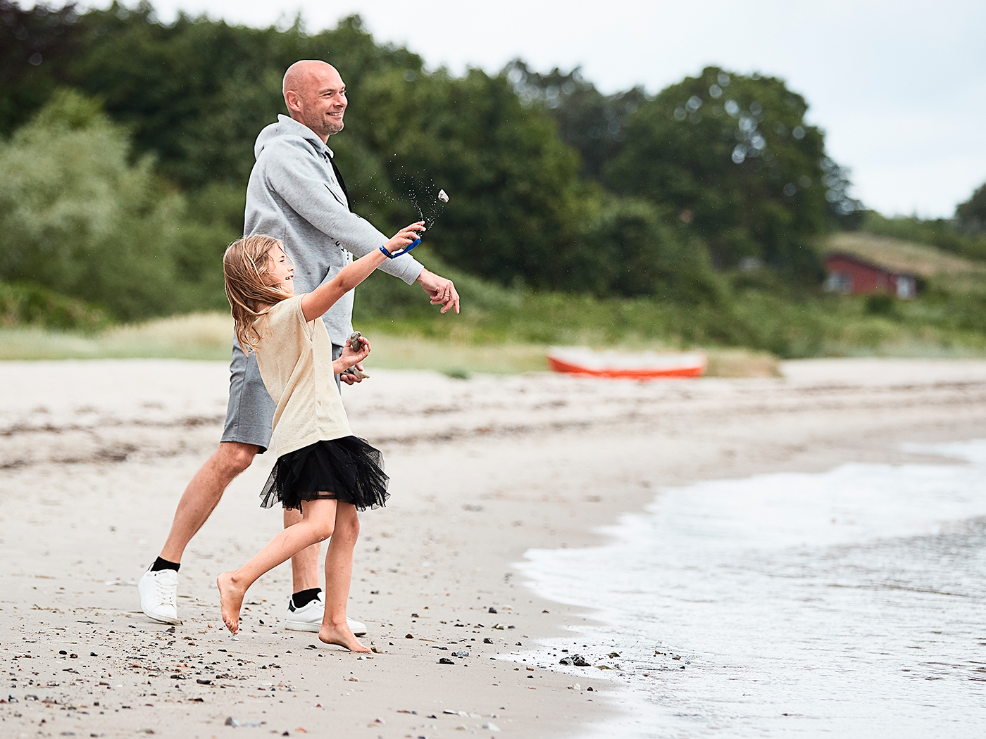 Far og datter på stranden kaster sten i havet