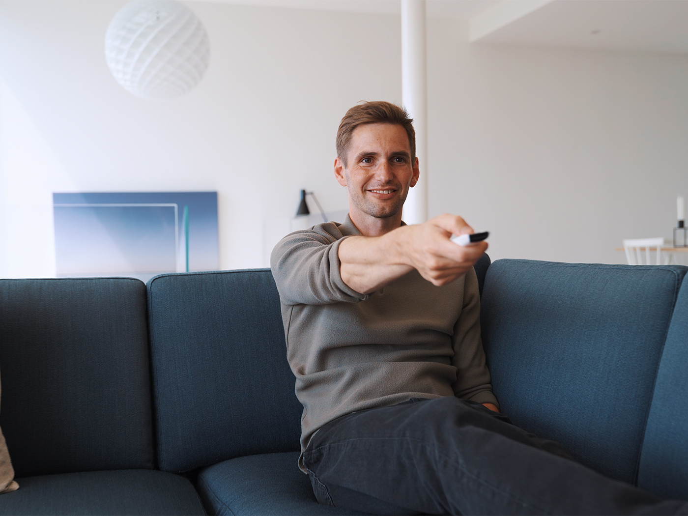 Mand sidder i sofa med fjernbetjening og streamer tv film og serier