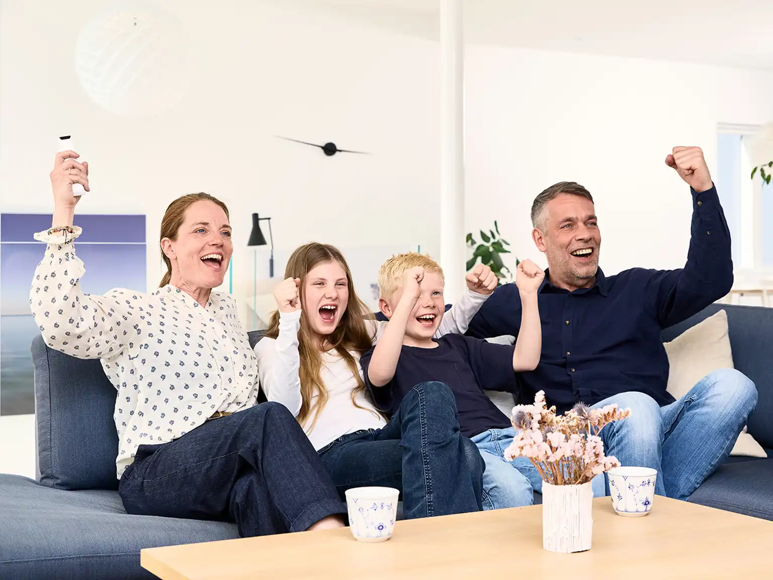 Familie sidder sammen i sofa og jubler med armene over hovedet mens de ser tv