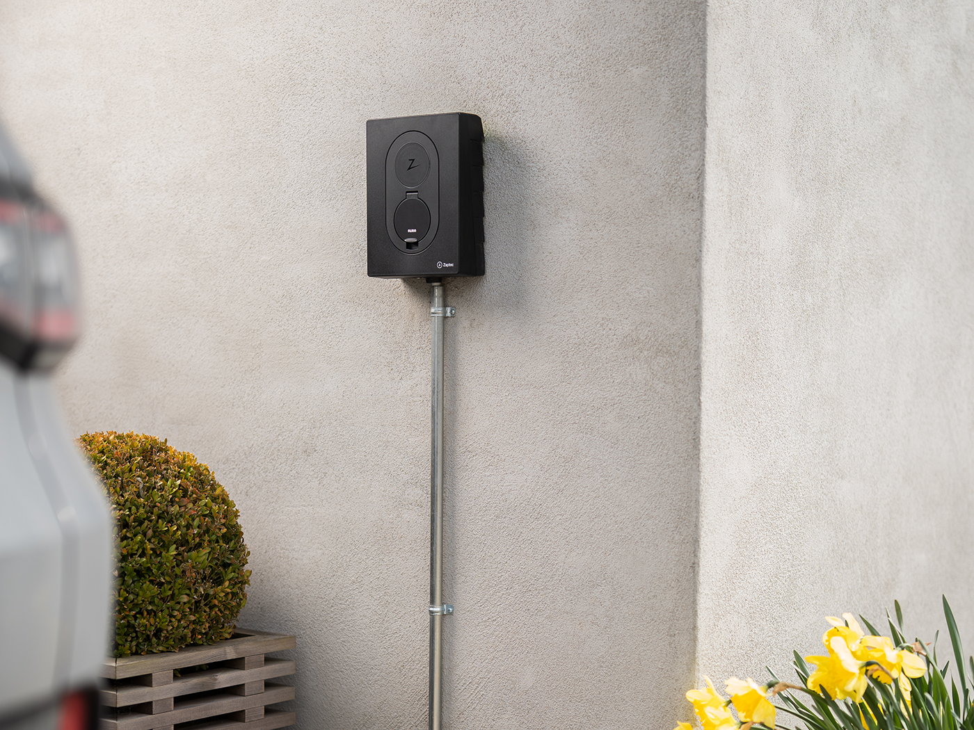 Ladeboks monteret på husets ydermur omgivet af elbil, buske og påskeliljer