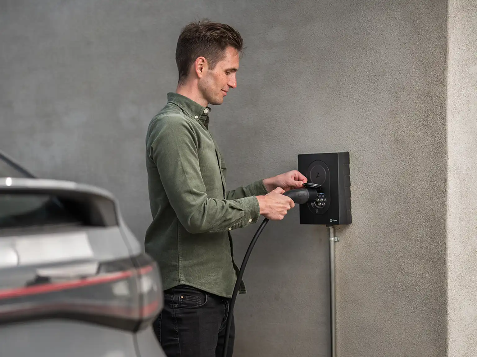 Mand der sætter ladekablet i ladeboksen for at oplade elbil