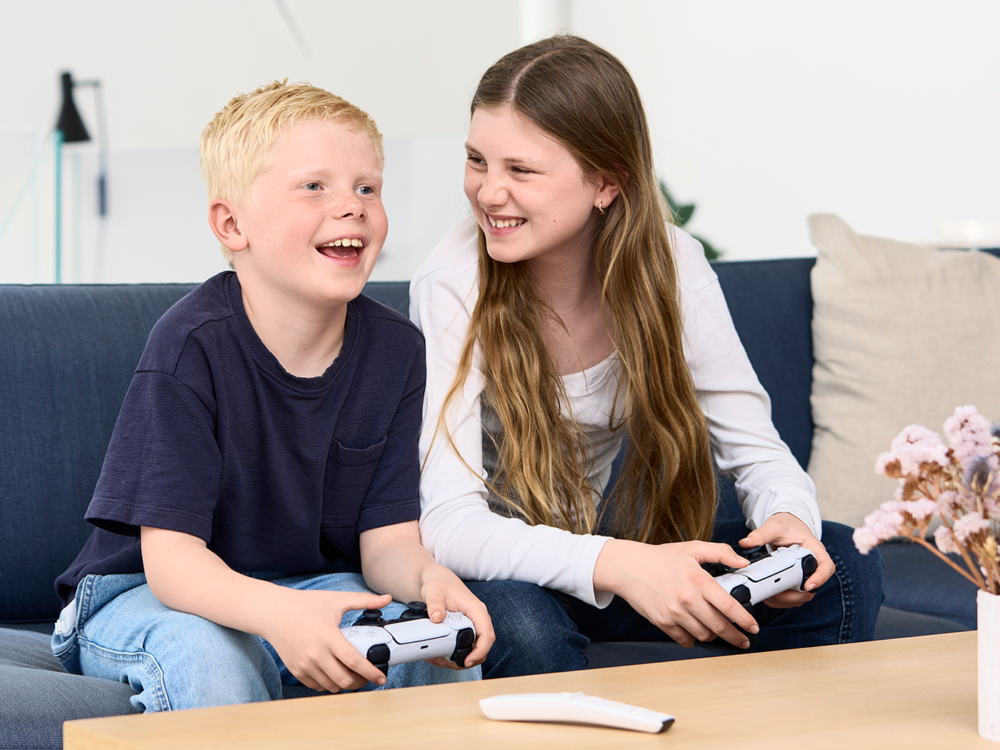Dreng og pige sidder i sofaen og griner mens de spiller konsolspil