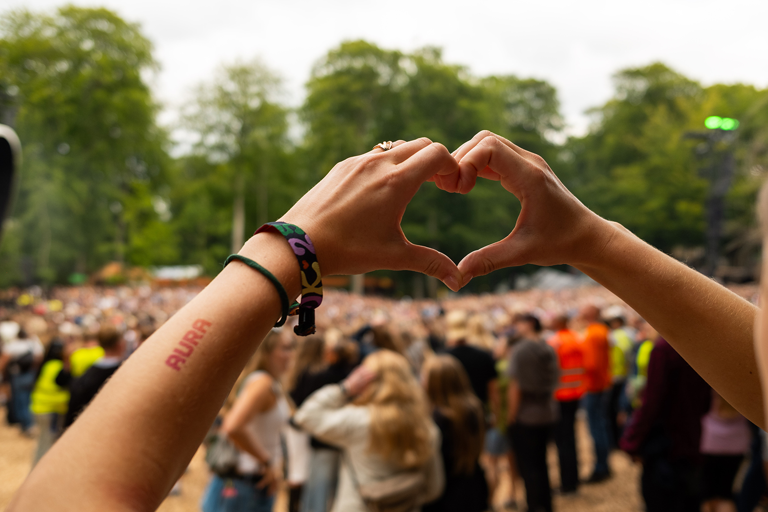 Hænder der former et hjerte på Smukfest med AURA tatovering på armen
