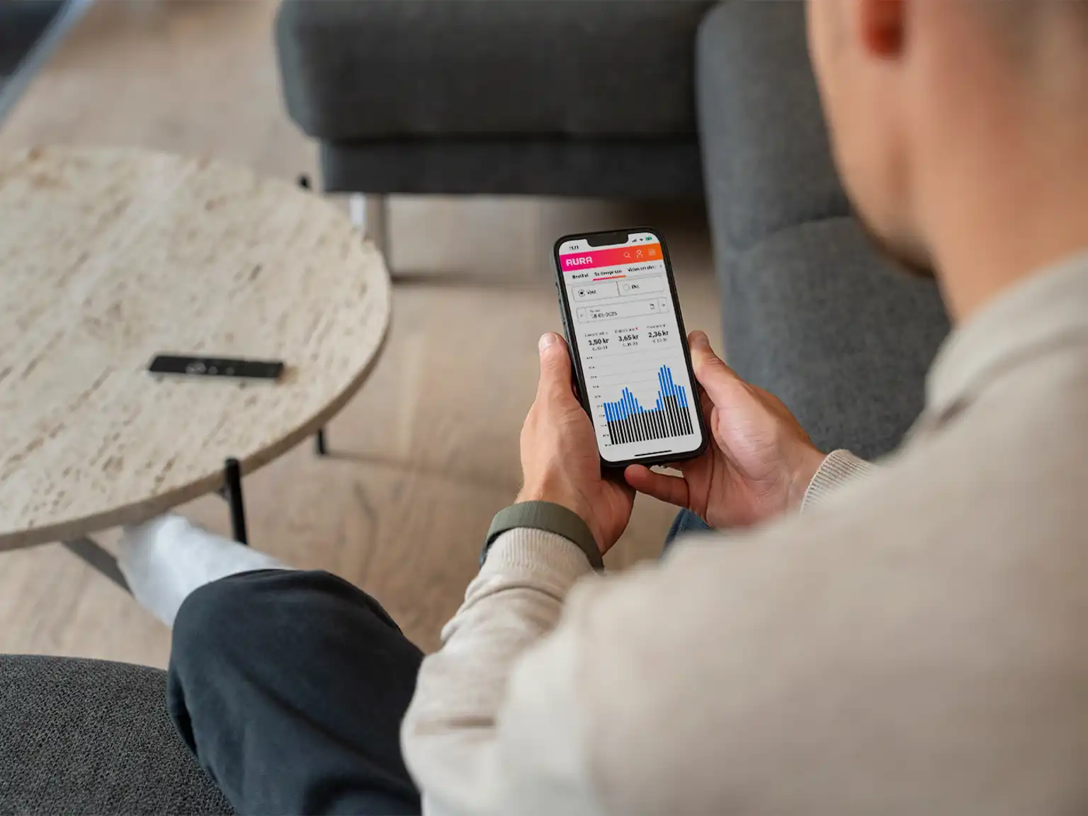 Mand sidder i en sofa med sin mobil og kigger på AURAs timeprisviser