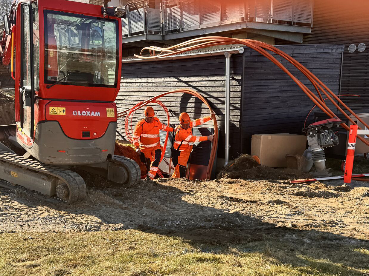 To mænd lægger fiberkabler i jorden langs en bygning