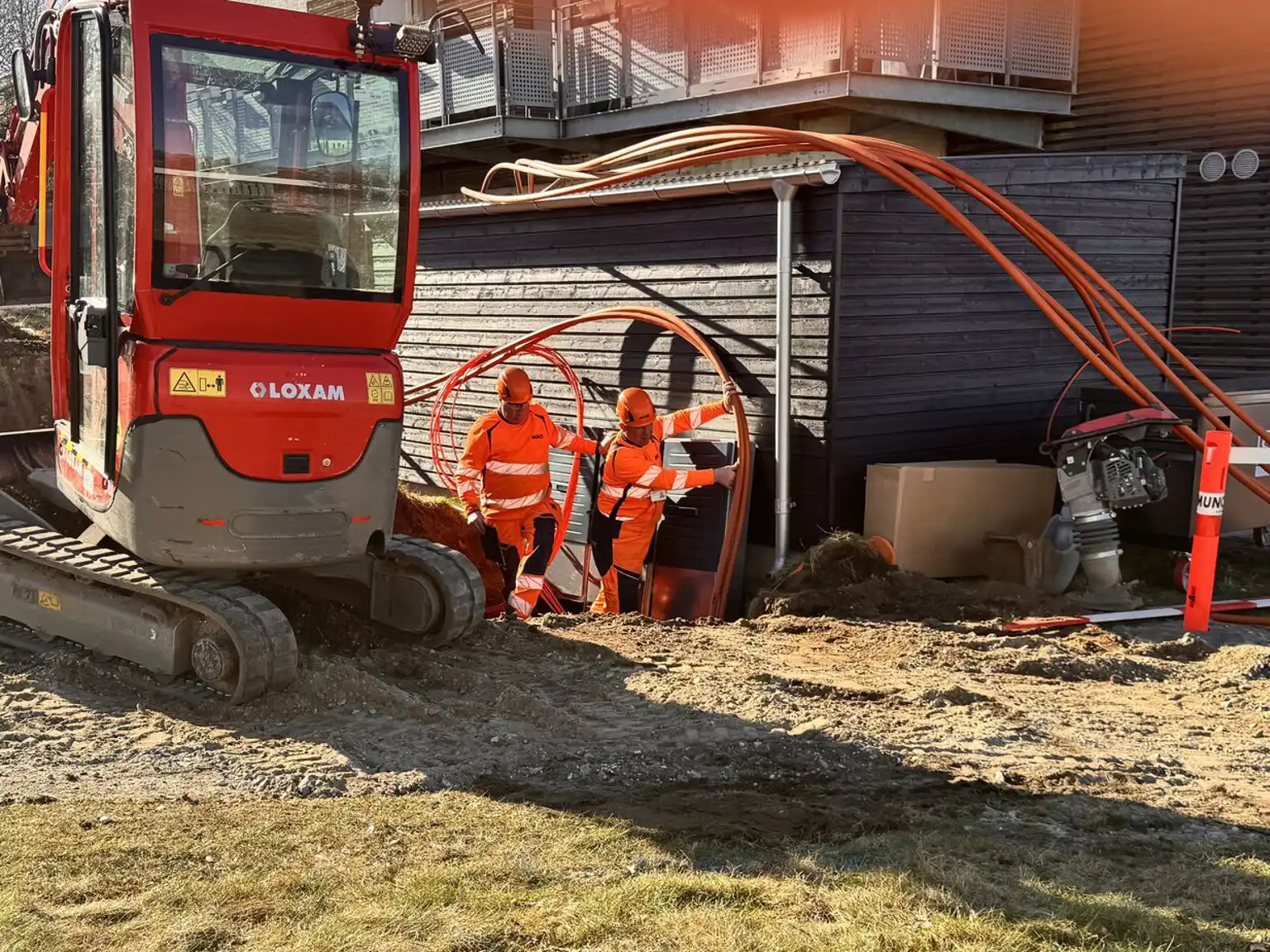 To mænd lægger fiberkabler i jorden langs en bygning