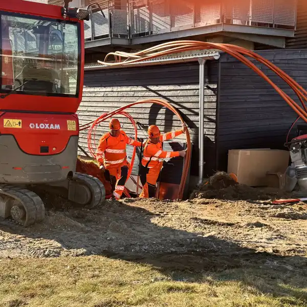 To mænd lægger fiberkabler i jorden langs en bygning