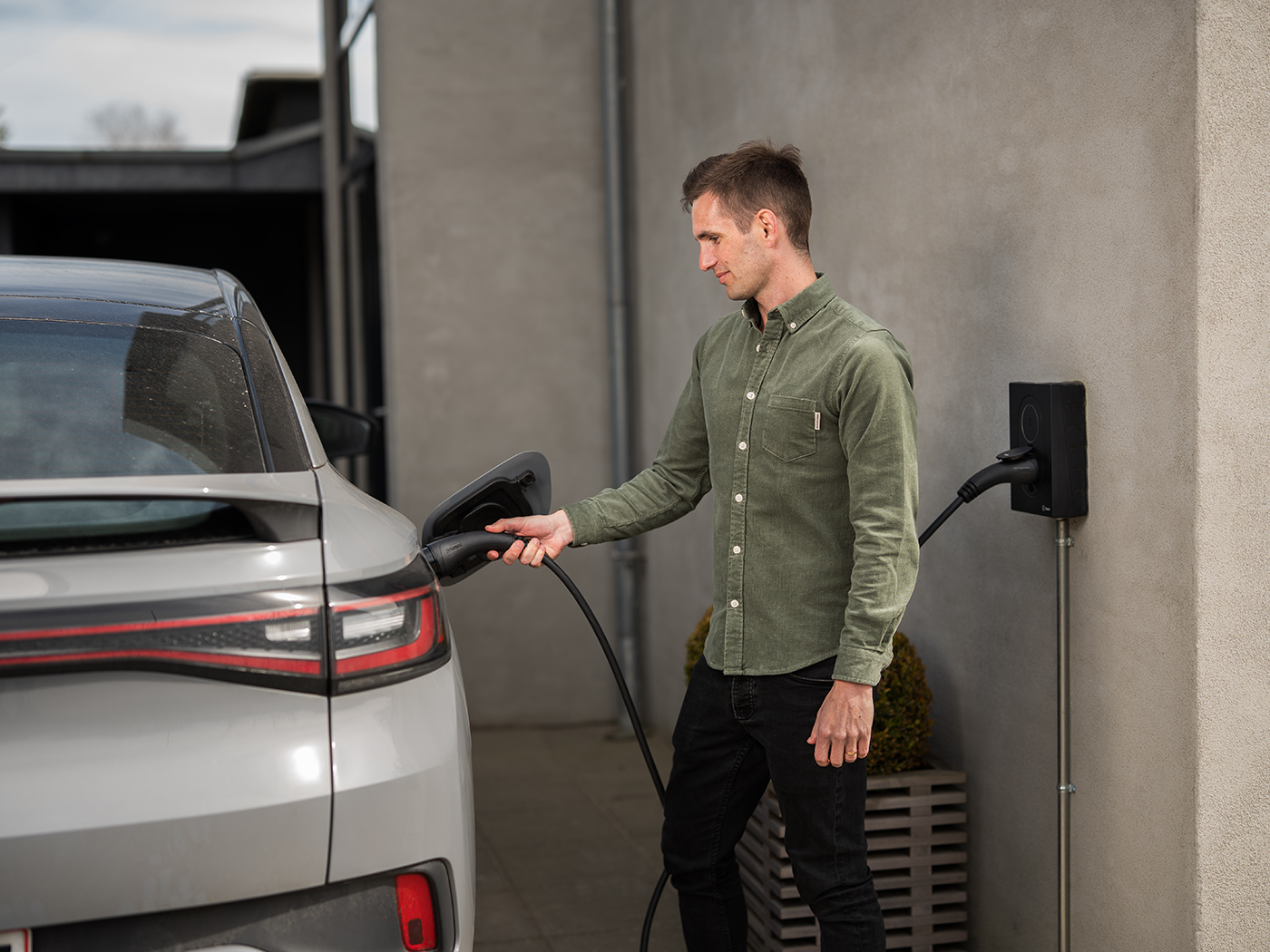 Mand der sætter ladekabel i sin elbil fra ladeboksen monteret på væggen af huset