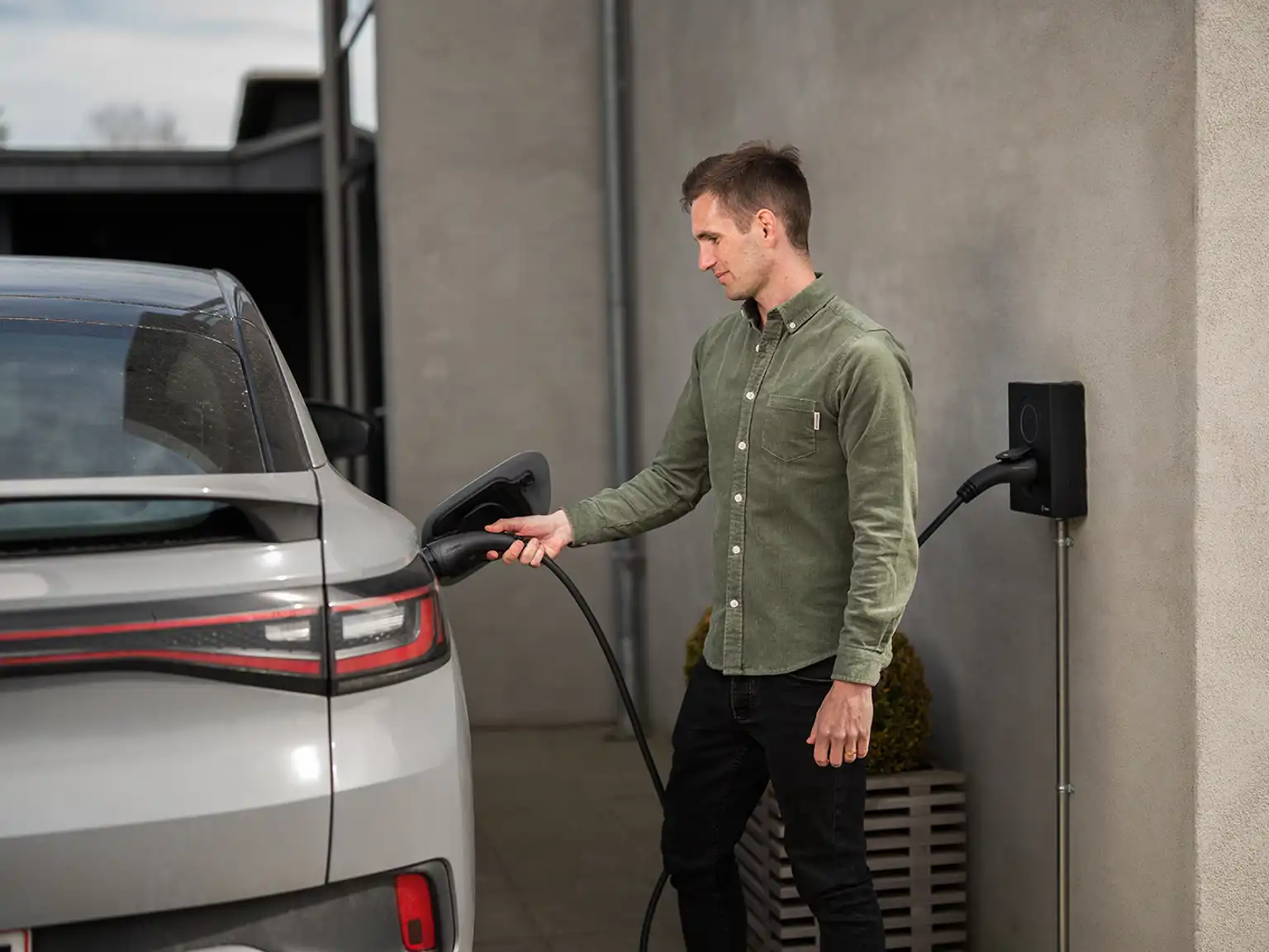 Mand der sætter ladekabel i sin elbil fra ladeboksen monteret på væggen af huset