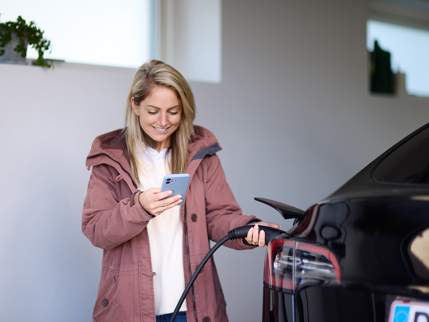 Kvinde sætter ladekabel i elbil og holder mobil