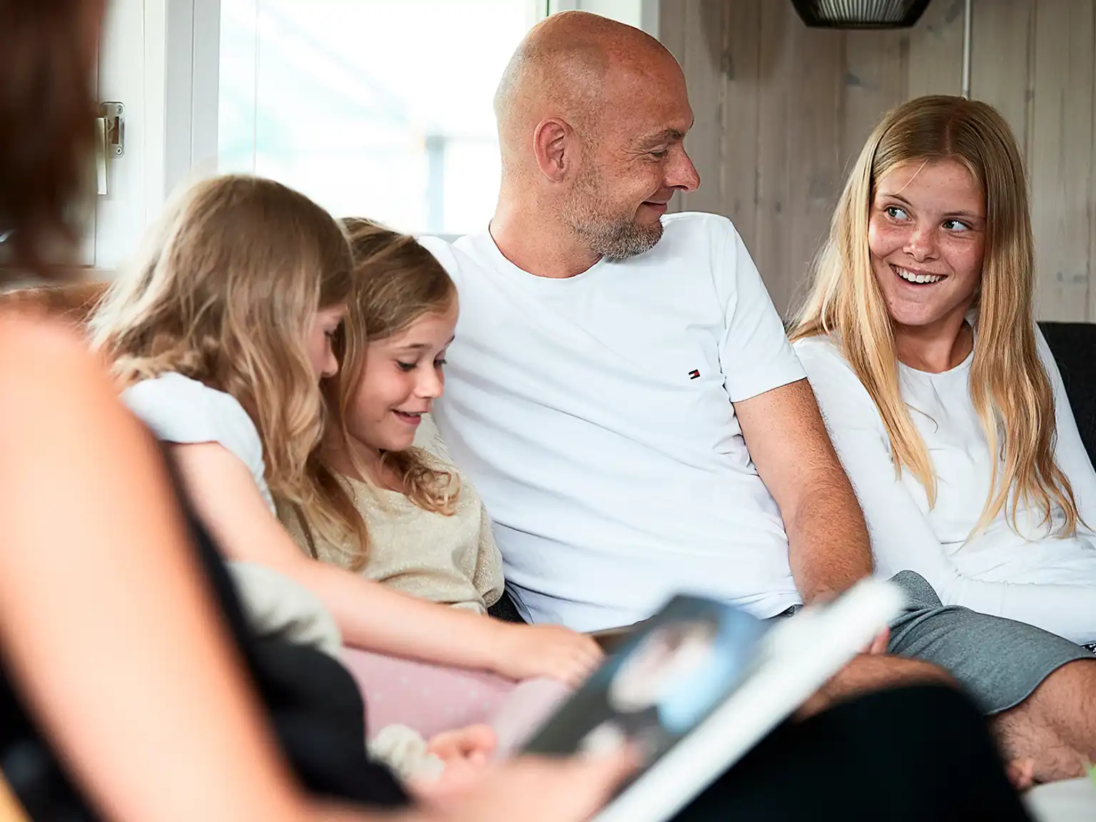 Familie sidder sammen i en sofa i sommerhus og ser tablet og læser bøger