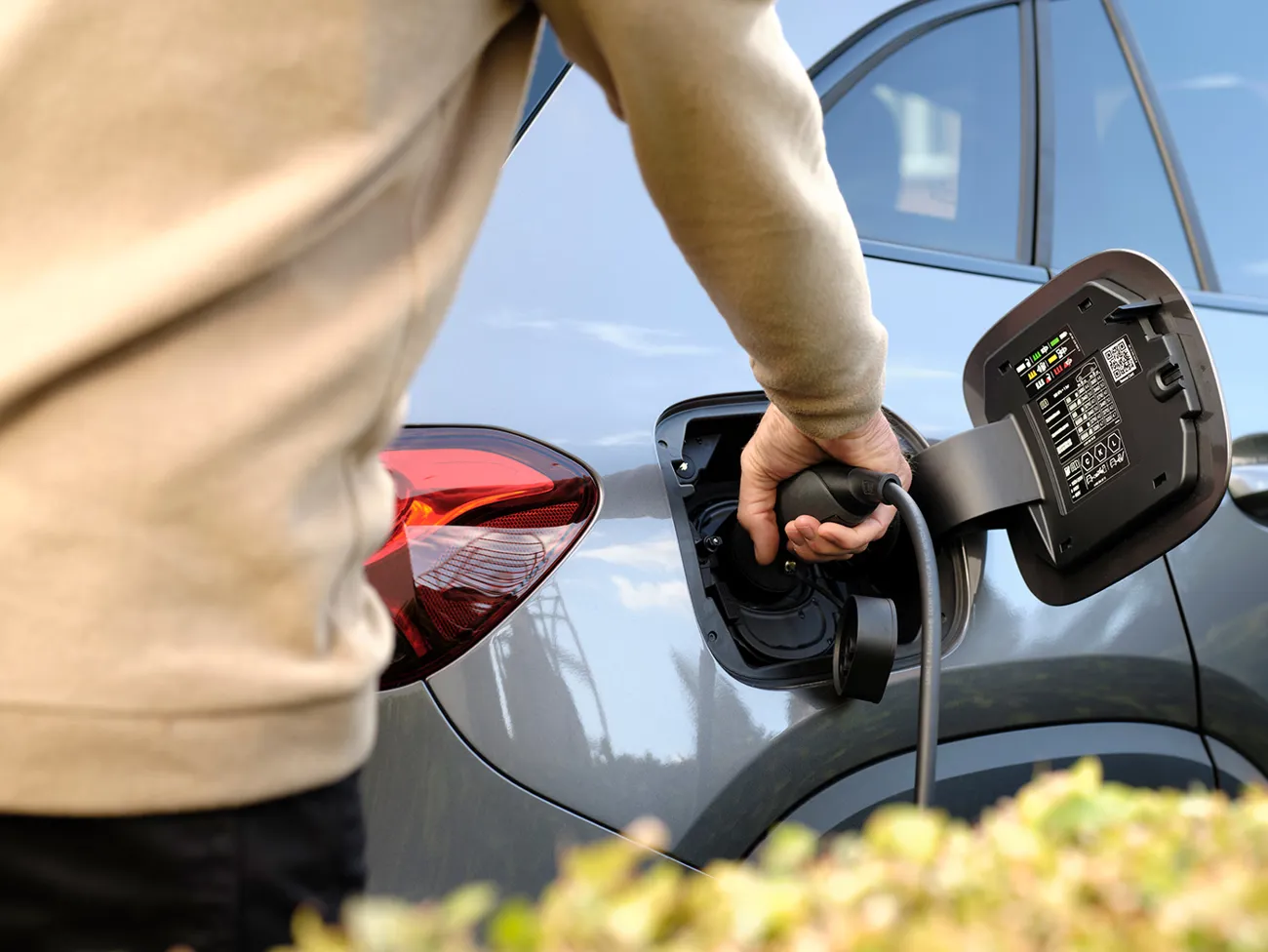 Mand sætter ladekabel i stikket til elbil for at oplade hjemme