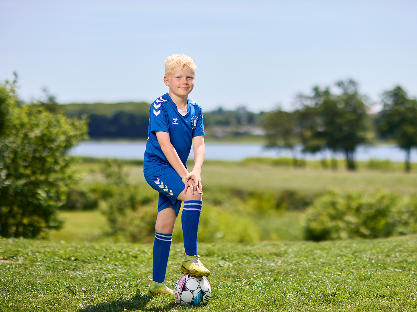 Dreng står i haven i fodboldtøj med foden på fodbold