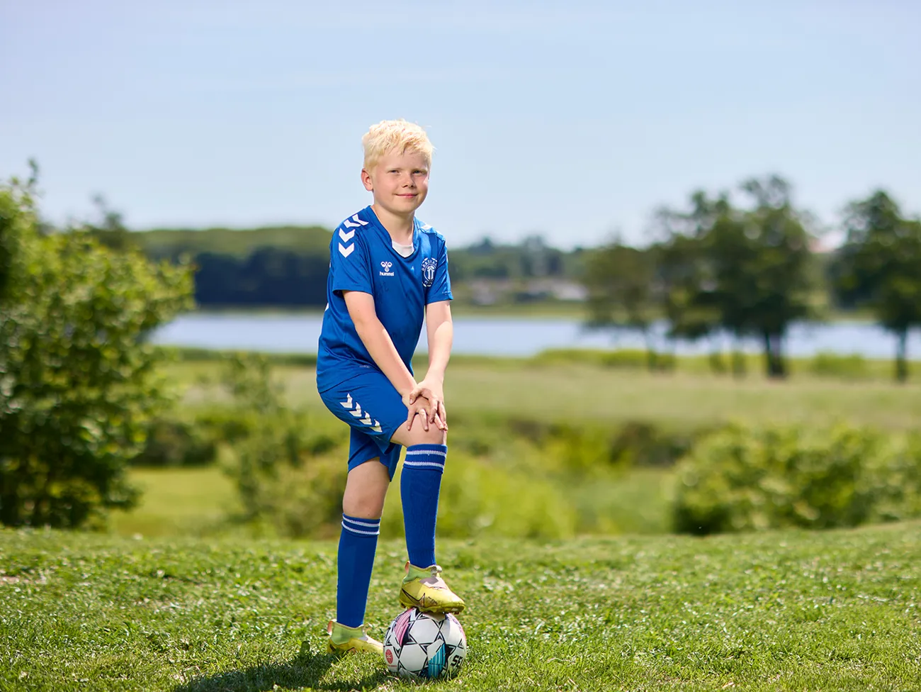 Dreng står i haven i fodboldtøj med foden på fodbold
