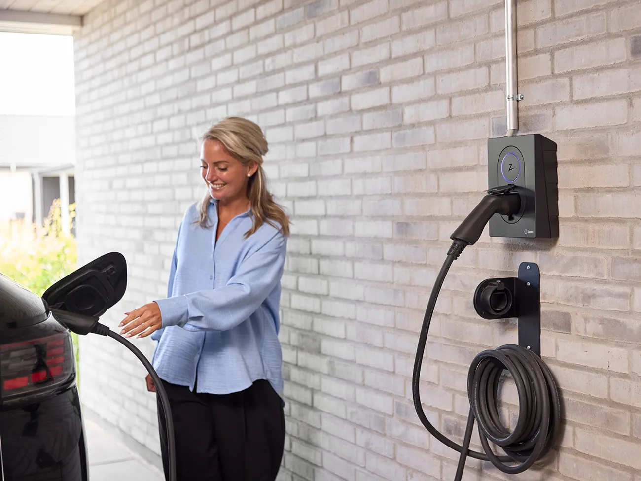Kvinde sætter ladekabel i elbil og gør klar til opladning af batteriet