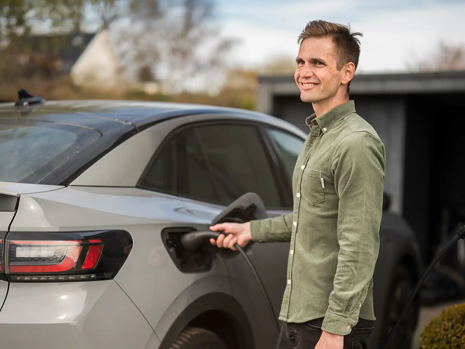 Mand står og smiler mens han lader elbilen