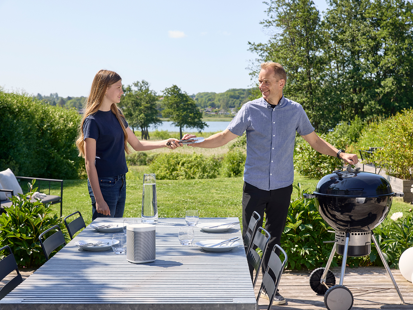 Datter rækker sin far grilltang til kuglegrillen på terrassen