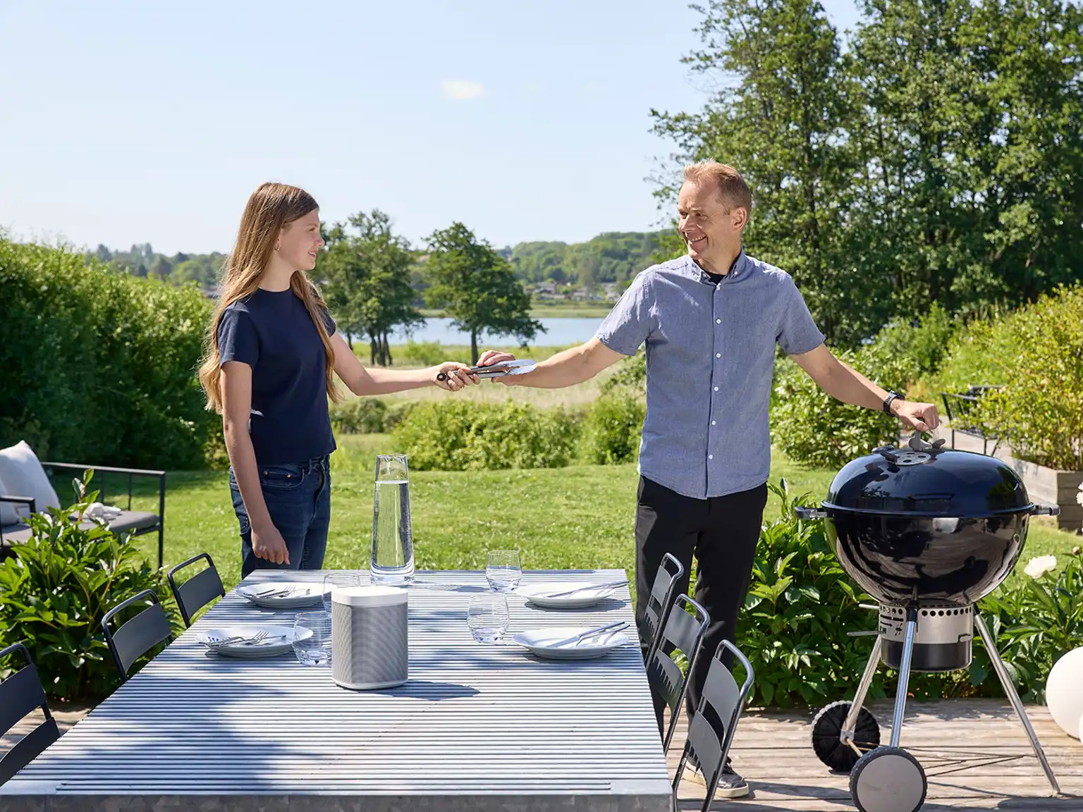 Datter rækker sin far grilltang til kuglegrillen på terrassen