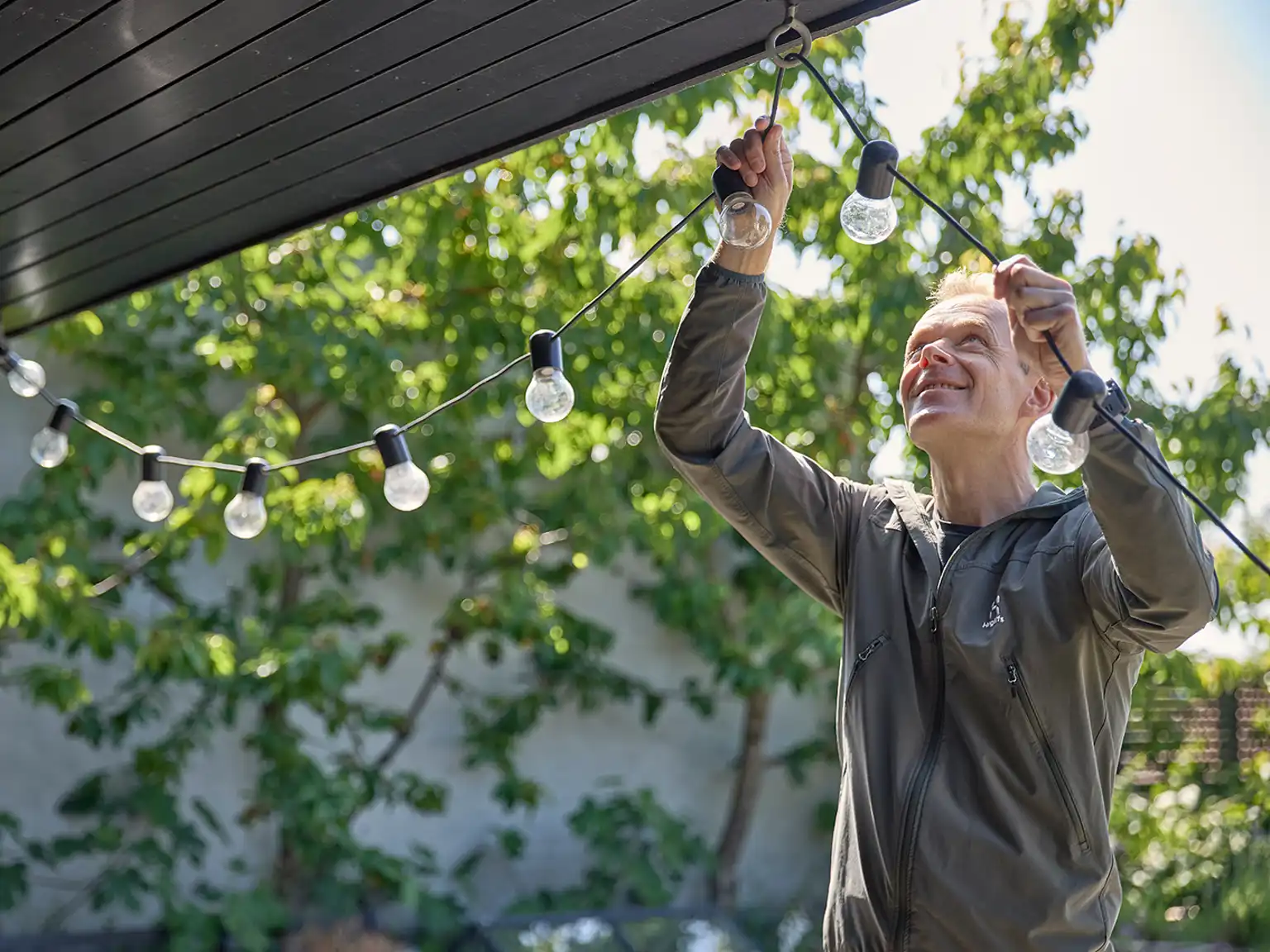 Mand hænger lyskæde op i kroge på husets udhæng