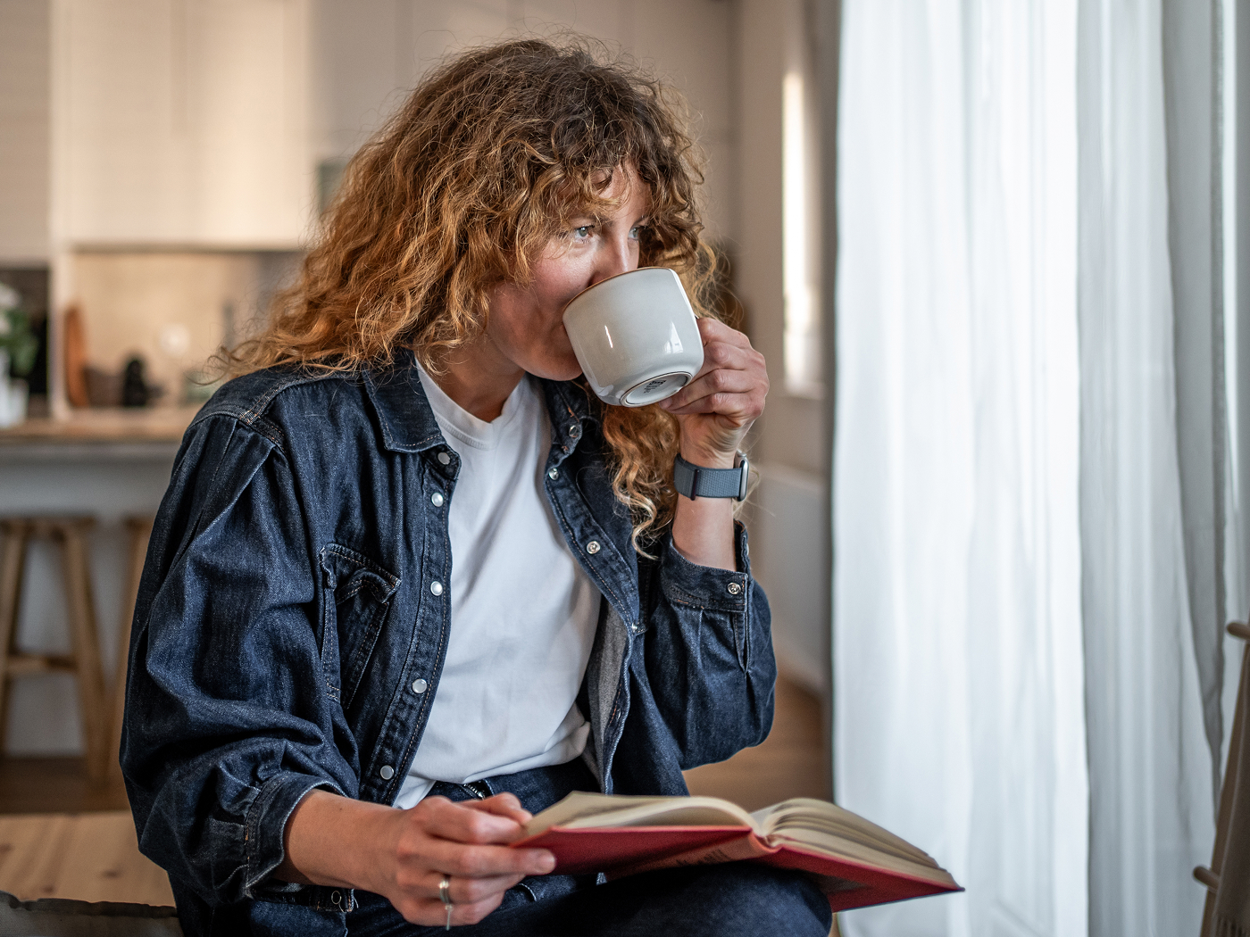 Kvinde der drikker af kaffekop og kigger ud af vinduet