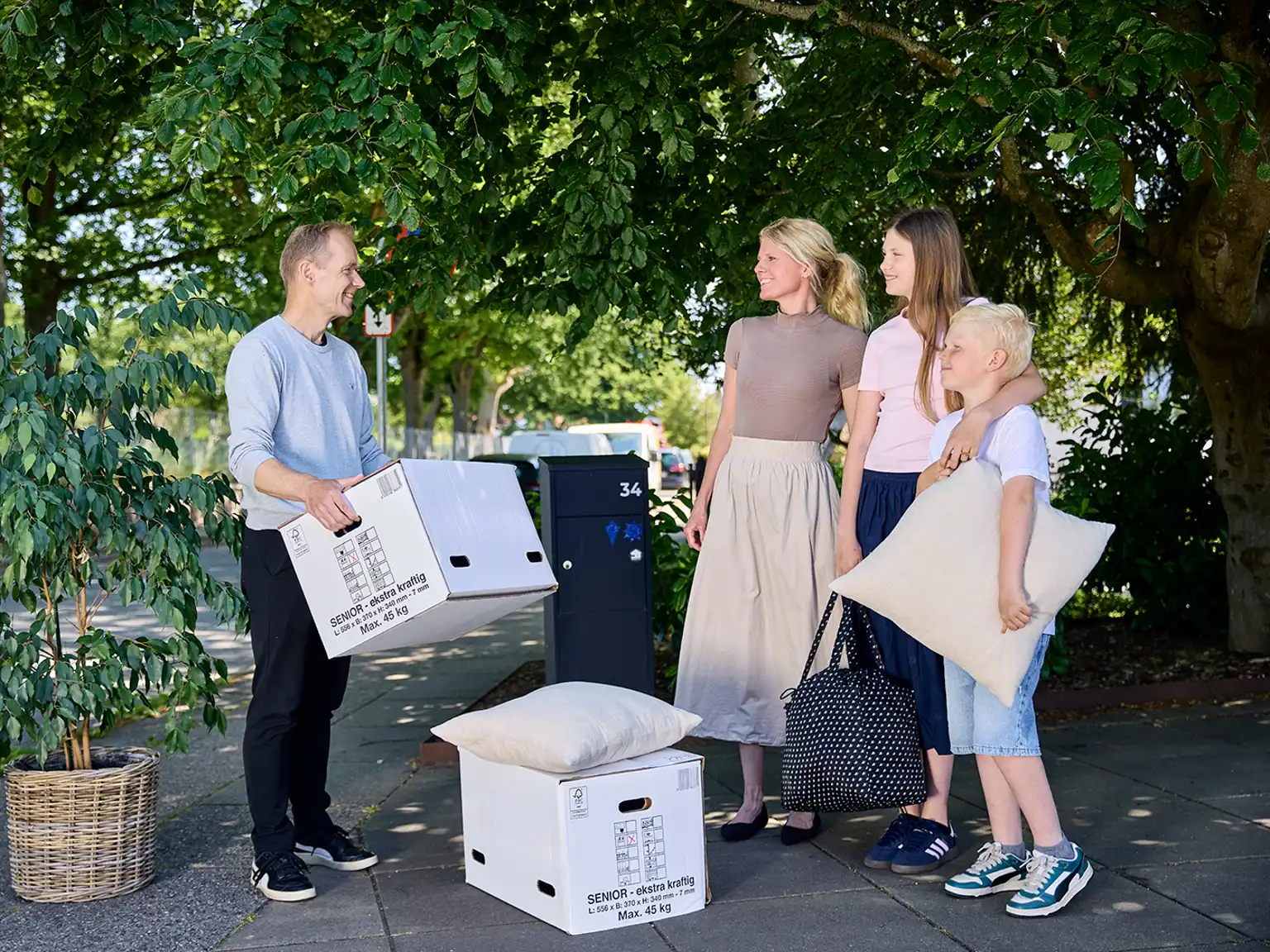 Familie på to voksne og to børn står med flyttekasser og oppakning ved deres postkasse