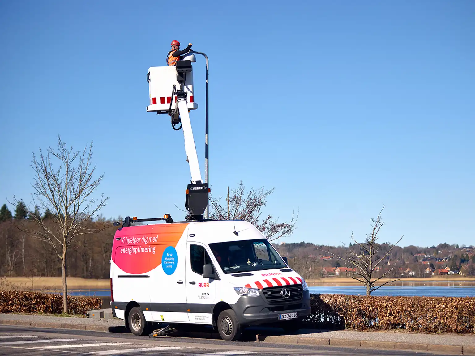 AURA bil holder parkeret med medarbejder i kran, som servicerer gadelys langs vejen