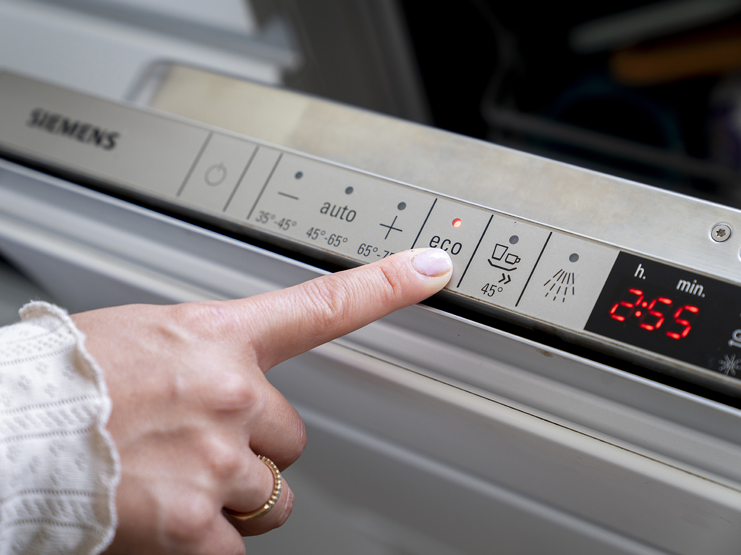 En person peger på en digital skærm på en opvaskemaskine og fremhæver dens miljøvenlige energibesparende funktioner