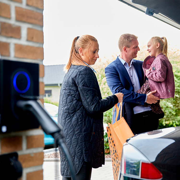 Familie tømmer elbilen for indkøbsnet, mens den oplader hjemme via deres ladeboks
