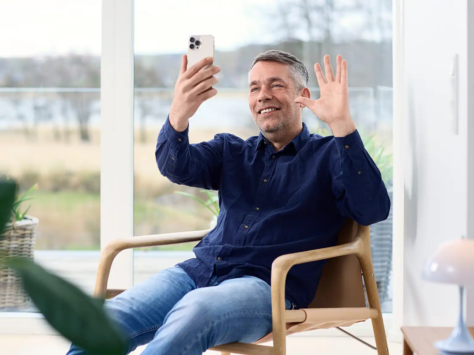 Mand sidder i stol og vinker til mobilkameraet under et opkald