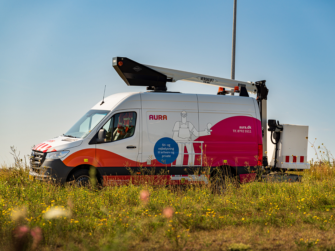 Bil fra AURA Installation holder parkeret ved en markvej nær gadelys