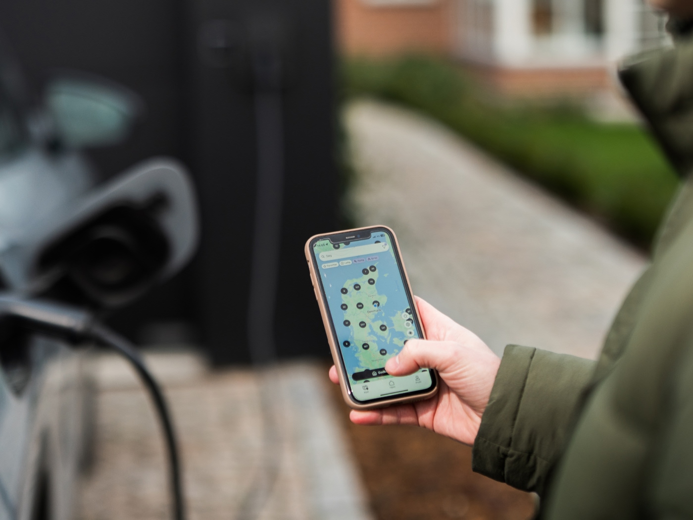 Mand står og kigger på et kort over ladestandere på telefonen mens bilen lader.